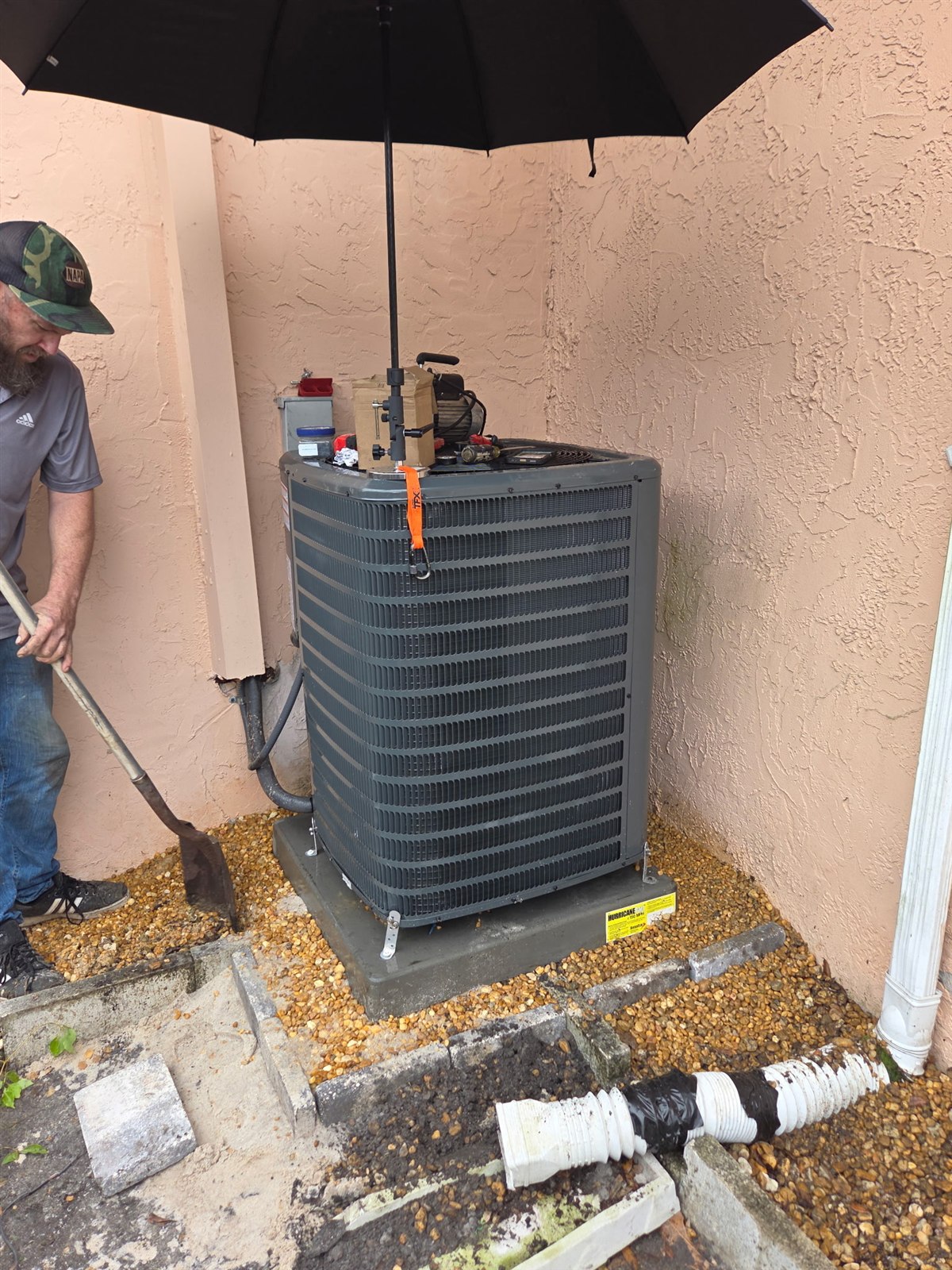 Technician servicing an outdoor air-conditioning condenser with diagnostic gauges